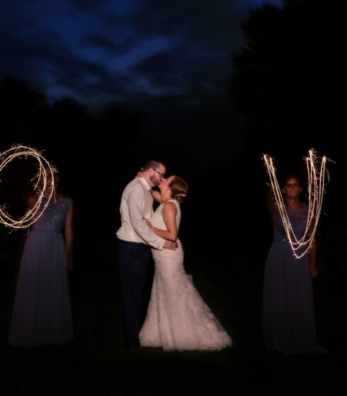 Bride and groom kissing while brides maids spell out love in sparklers.