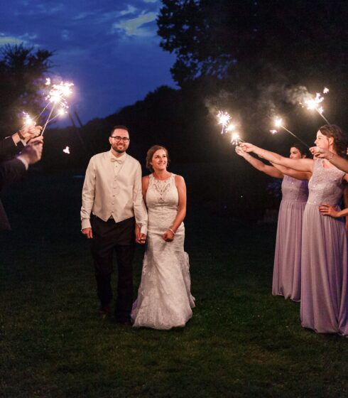 Bride and groom holding hands while walking through a tunnel of sparklers held by the wedding party.